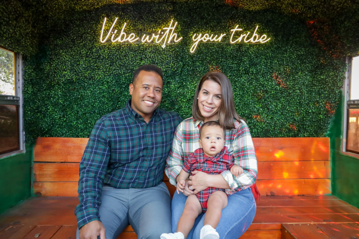 Smiling couple with a baby on a bench, neon sign text above.
