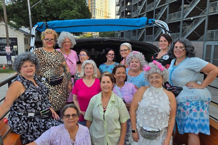 A group of people dressed eccentrically on a wooden platform, with buildings in the background.