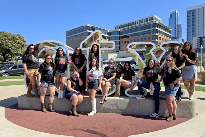 Group of women posing in front of large 'ATX' letters with buildings in the background.