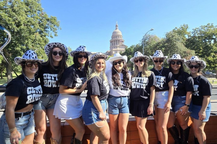 Group of women in cowboy hats and boots posing outdoors with a domed building in the background.